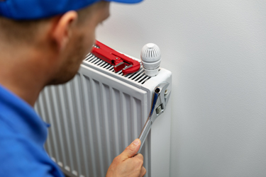 emergency plumber in Sheffield and surrounding areas plumber in blue cap fixing radiator using wrench