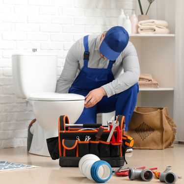 emergency plumber in Sheffield and surrounding areas plumber fixing broken toilet with orange and black toolbox and wearing a blue cap