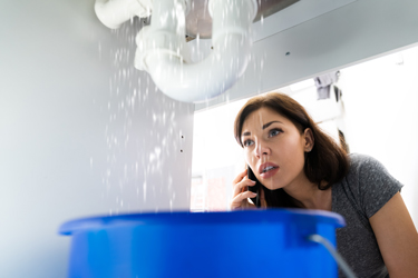 emergency plumber in Sheffield and surrounding areas woman on the phone for emergency plumber call out with sink pipes leaking into blue bucket